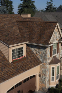 Aerial view of home with stone exterior, brown garage door, and brown asphalt shingle roofing.