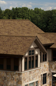 Aerial view of luxurious home with stone exterior and brown asphalt shingle roofing.