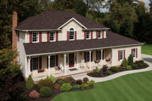 Large two-story single family home with long front porch, a large front lawn, and asphalt roofing.