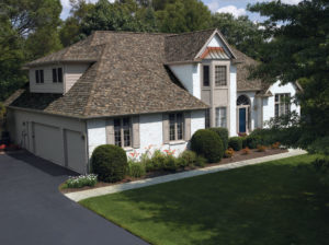 Exterior of luxurious single family home with brown roofing, landscaping, and a three-car garage.