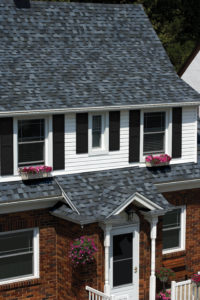 Exterior view of single family home with modest porch, black window shutters, and gray shingle roofing