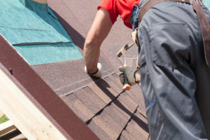 Roofer builder worker installing roofing shingles using a hammer 