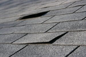 A close-up image of a damaged asphalt shingle roof with shingles that are coming loose.