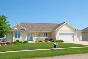 An upscale ranch home with stucco siding, manicured lawn, and a brown asphalt shingle roof.