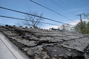 View of roof with old and damaged shingles. Blue sky in background.